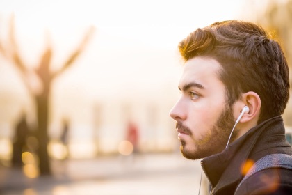 Male side profile with ear bud headphones listening to sounds via an app.