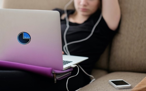 Girl sitting on lounge with her computer listening to an audiobook.