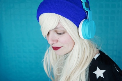 Female with blue beanie wearing headphones listening to a podcast.